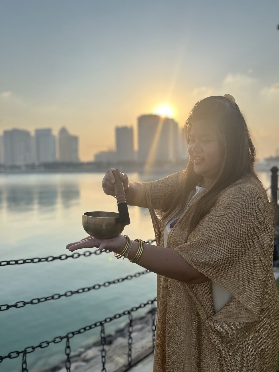Vivi playing a singing bowl by the water at sunset in Doha